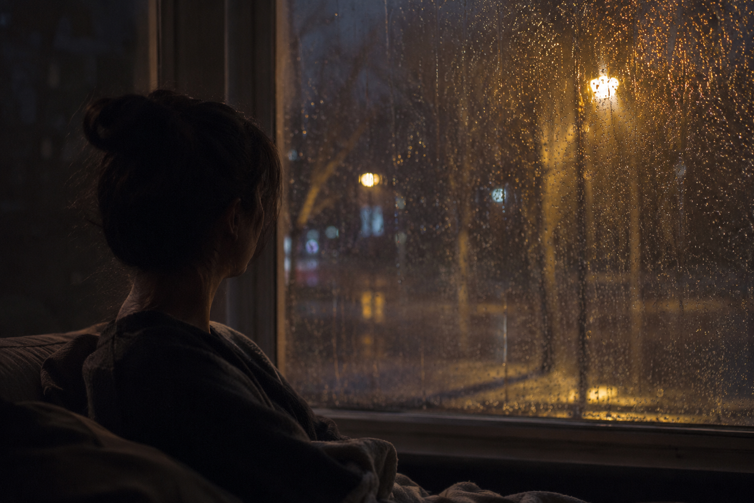 雨の夜、窓の外の街灯の光を、部屋の中からひとりで眺めている様子